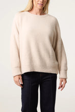 Load image into Gallery viewer, A woman wearing a fuzzy, oversized crewneck sweater in a light cream color, paired with dark blue jeans, against a plain light background.